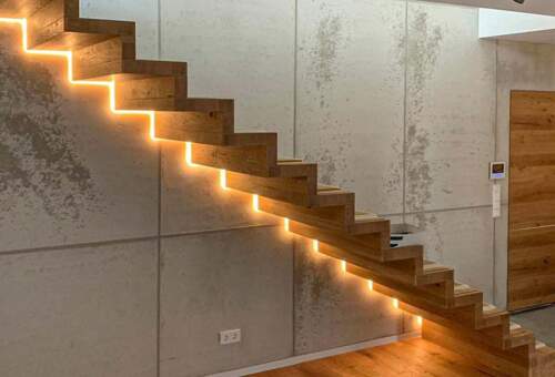 Raum mit beleuchteter Holztreppe vor mit Beton beschichteter Wand